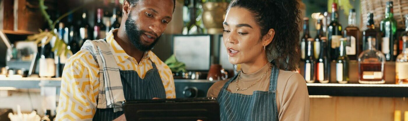Restaurant, teamwork and people on tablet for training for inventory, menu items and checklist by bar. Alcohol, business and man with woman on digital tech for hospitality, service and online order